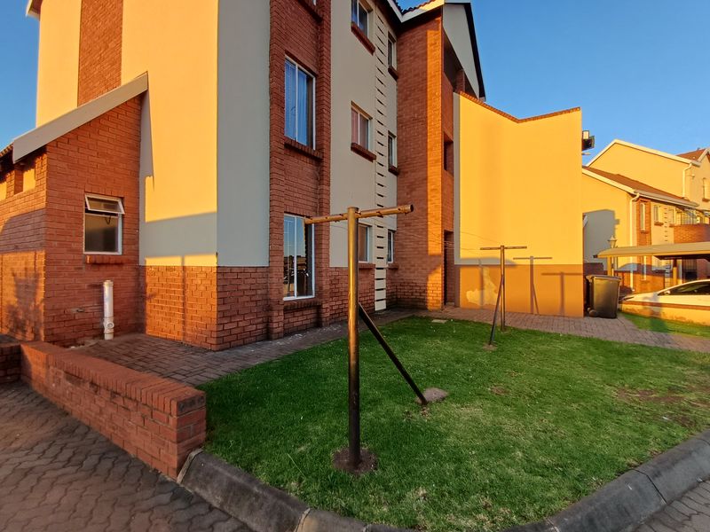 Rear exterior view of the apartment building featuring a small lawn, paved area, and brick facade with visible maintenance required on the wall paint.