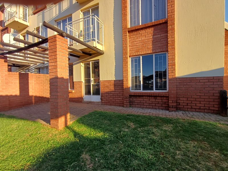 Rear exterior view of the apartment featuring a paved patio area, timber pergola, and a small balcony with metal railings.