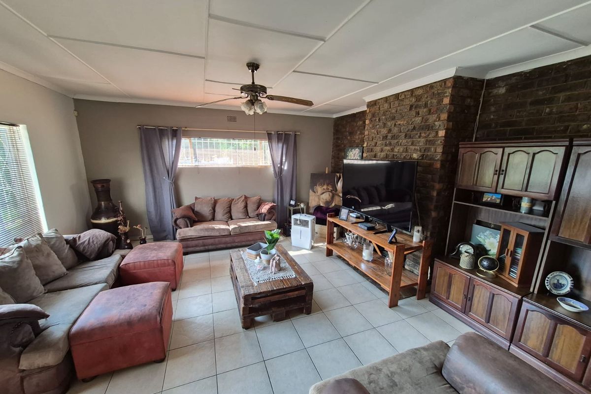 Spacious living room featuring a prominent face-brick fireplace, tiled flooring, and a ceiling fan, offering a comfortable and traditional living space.