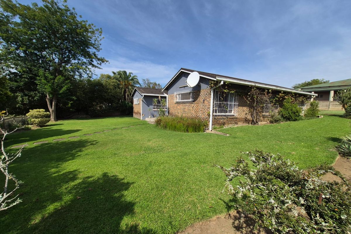 A spacious rear garden featuring a well-maintained lawn, mature trees, and a view of the brick-built house exterior with security bars on windows.