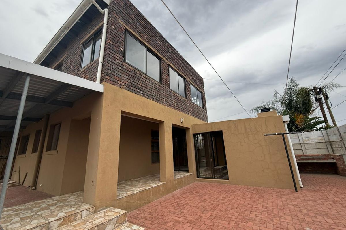 Rear exterior view of a two-story house featuring a paved courtyard, covered patio area, and built-in braai facility.
