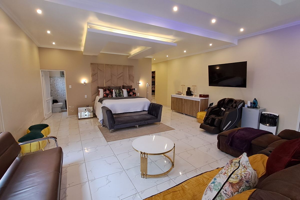 Spacious master bedroom featuring a tray ceiling with recessed lighting, polished porcelain floor tiles, and a large upholstered headboard.