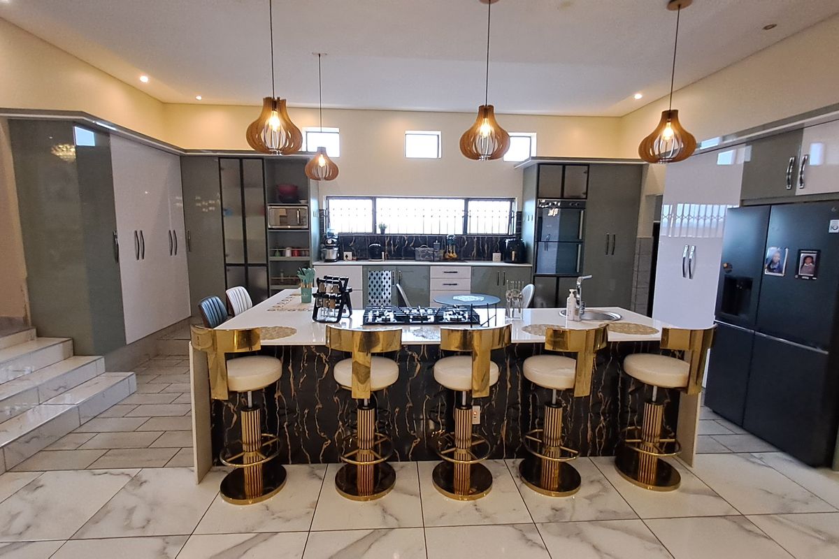 Modern open-plan kitchen featuring a large central island with a gas hob, sleek cabinetry, marble-look flooring, and contemporary pendant lighting.