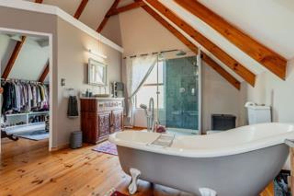 Spacious attic-style bathroom featuring exposed timber beams, a freestanding clawfoot bathtub, a glass-enclosed shower, and a vanity unit, with an adjoining walk-in closet.