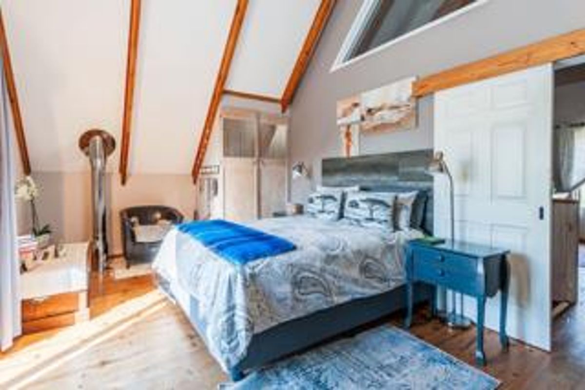 A cozy bedroom featuring a vaulted ceiling with exposed timber beams, wooden flooring, and a sliding door entrance.