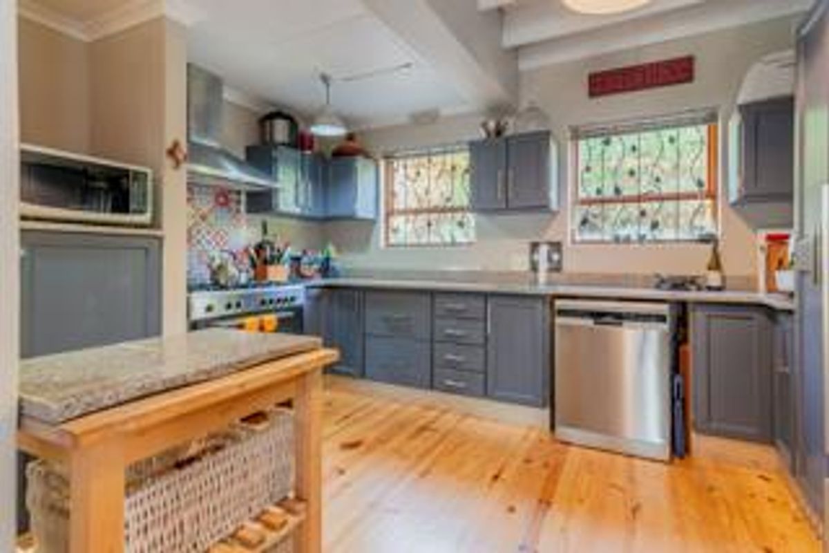 A functional kitchen featuring grey cabinetry, granite countertops, stainless steel appliances, and natural timber flooring.