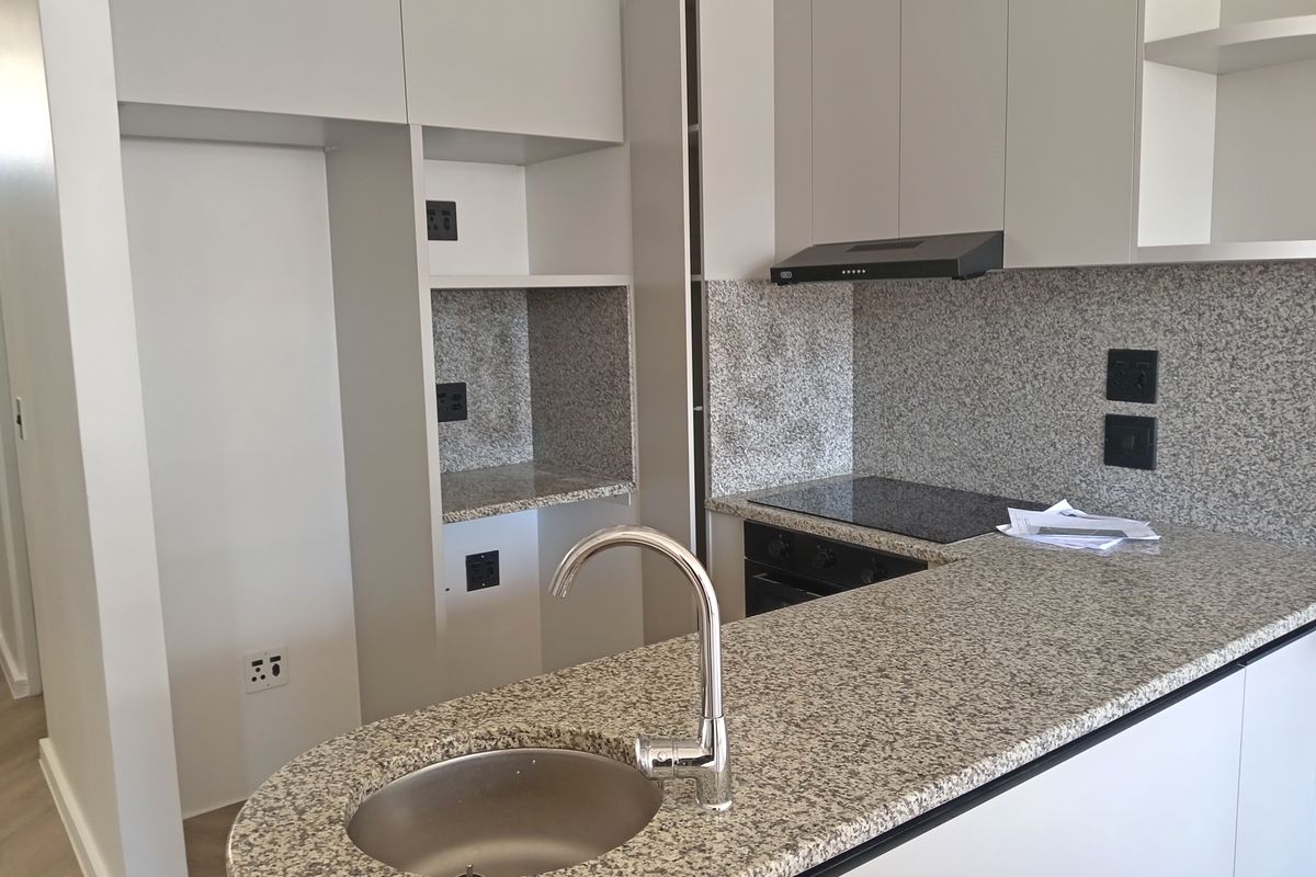 Modern kitchen featuring granite countertops, a built-in hob and oven, extractor fan, and a stainless steel sink with a contemporary faucet.