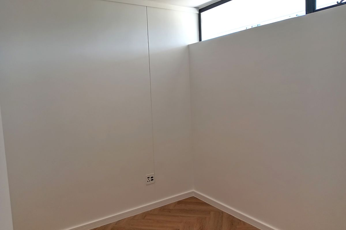 A bright, empty room featuring herringbone-patterned timber flooring, clean white walls, and a high-level clerestory window providing natural light.