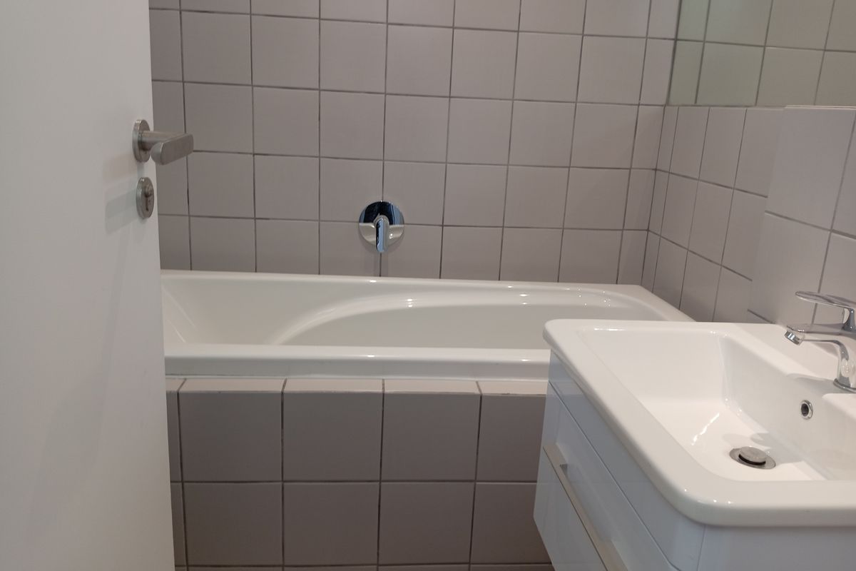 A clean, modern bathroom featuring a built-in bathtub with wall-mounted chrome fixtures and a contemporary vanity basin.