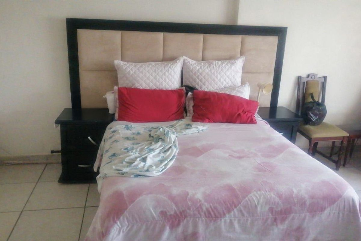 A bedroom featuring tiled flooring and a built-in headboard, showing signs of wear including visible wall cracks.