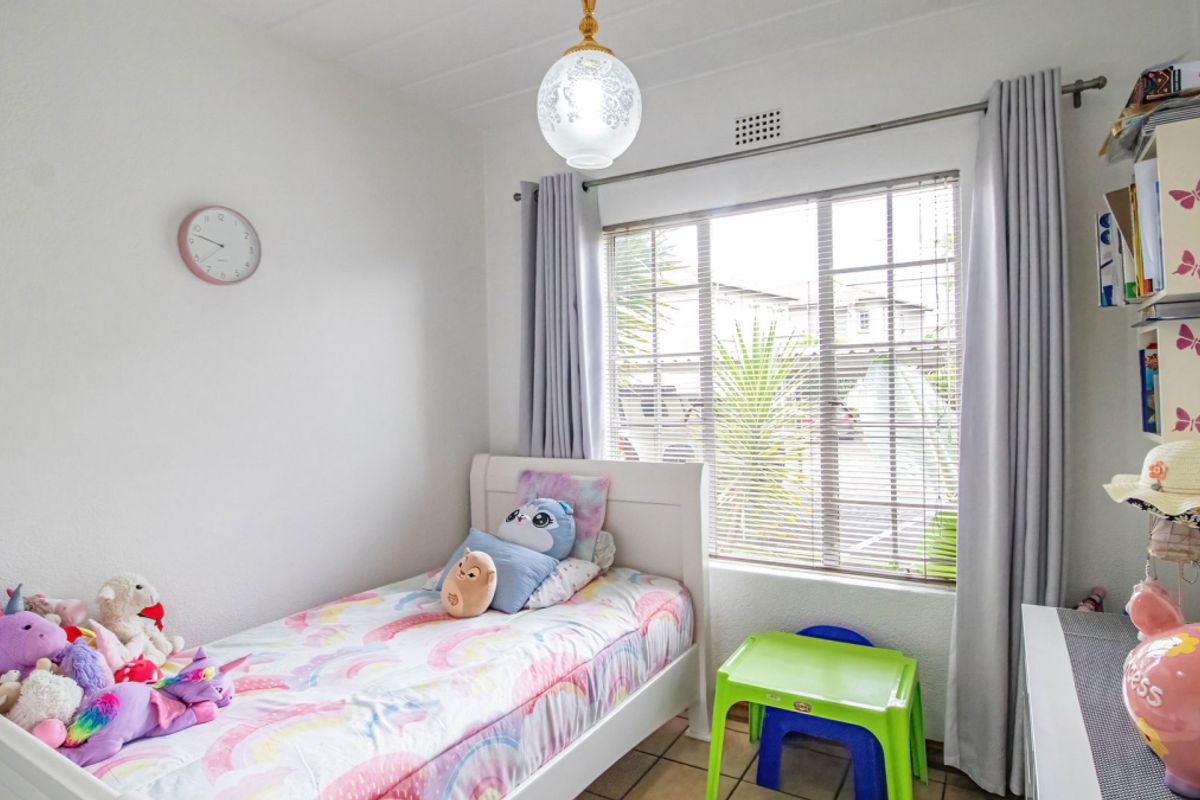 A functional bedroom featuring tiled flooring and a window with integrated blinds, providing natural light and ventilation.