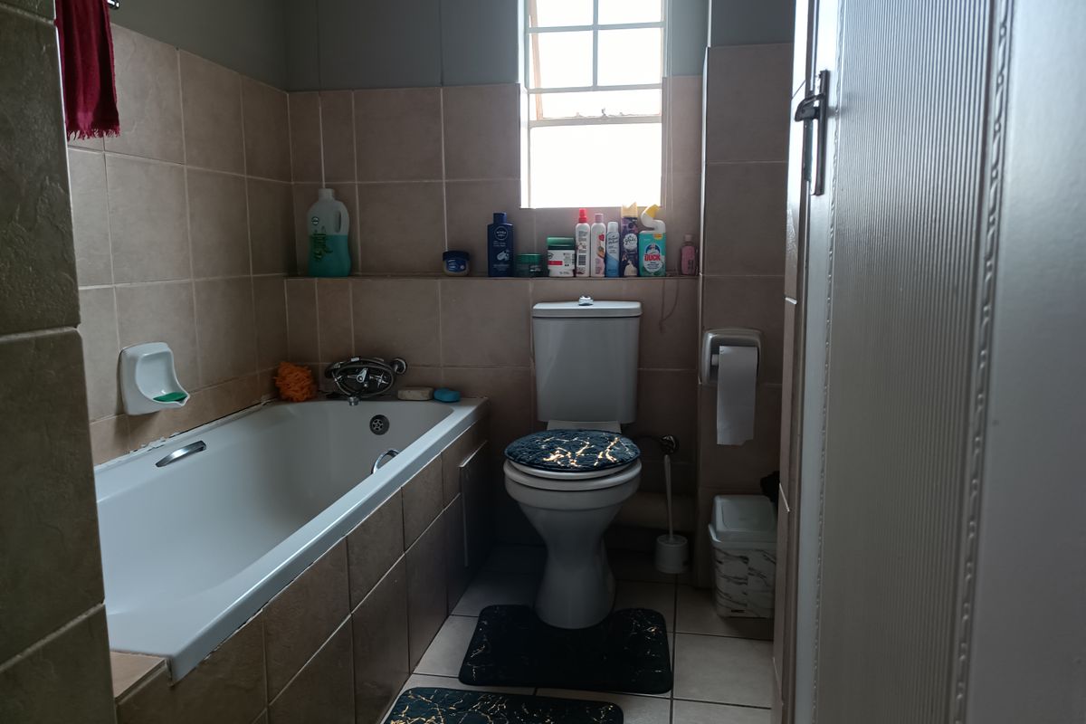A functional bathroom featuring a built-in bathtub, toilet, and neutral wall tiling with a recessed storage shelf.