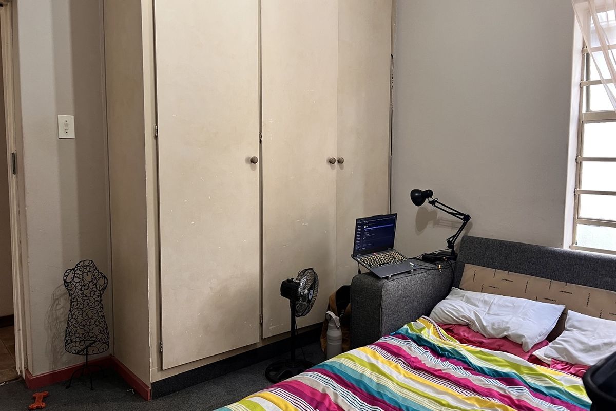 A bedroom featuring built-in cupboards and a window with security bars, offering a functional space with potential for cosmetic updates.