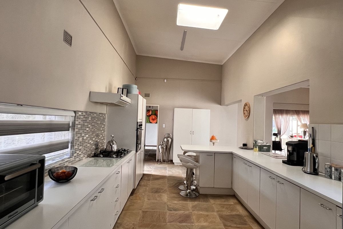 A spacious kitchen featuring white cabinetry, stone countertops, a gas hob, and a breakfast bar, with tiled flooring and a high ceiling.