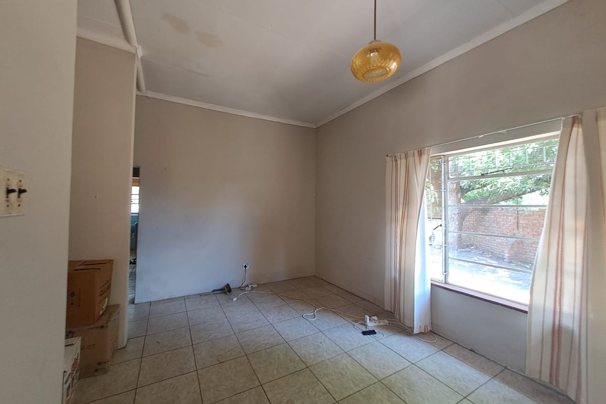 An empty living room featuring tiled flooring, a pendant light, and metal security bars on the window, showing signs of wear on the ceiling.