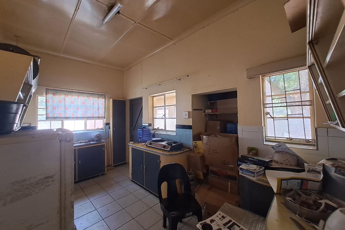 A dated kitchen featuring original cabinetry, tiled flooring, and security bars on the windows, offering significant potential for a modern renovation.