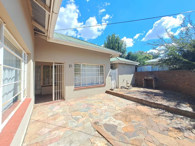 Rear exterior view featuring a stone paved patio area with a built-in brick braai and direct access to the home via a security gate.
