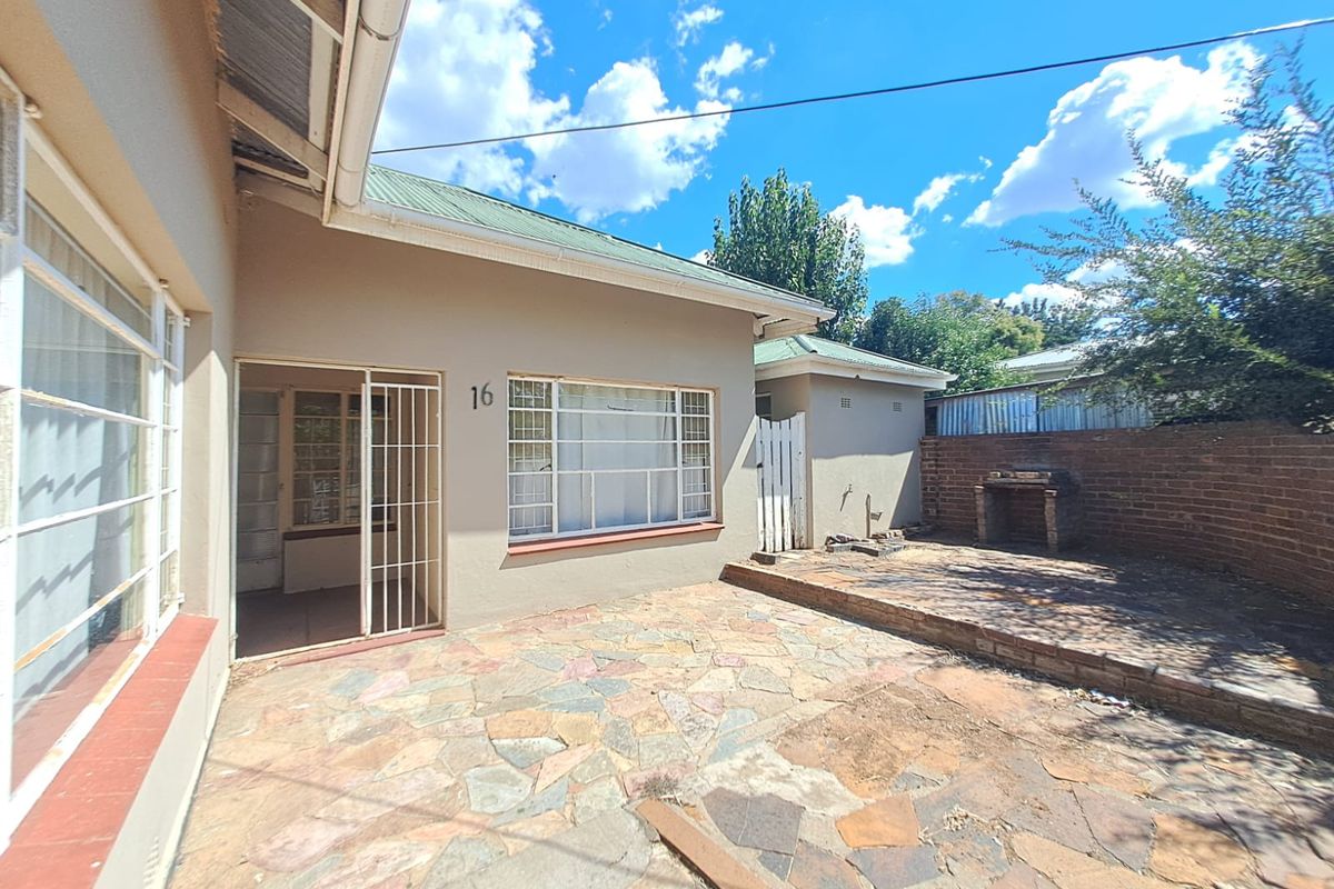 Rear exterior view featuring a stone paved patio area with a built-in brick braai and direct access to the home via a security gate.