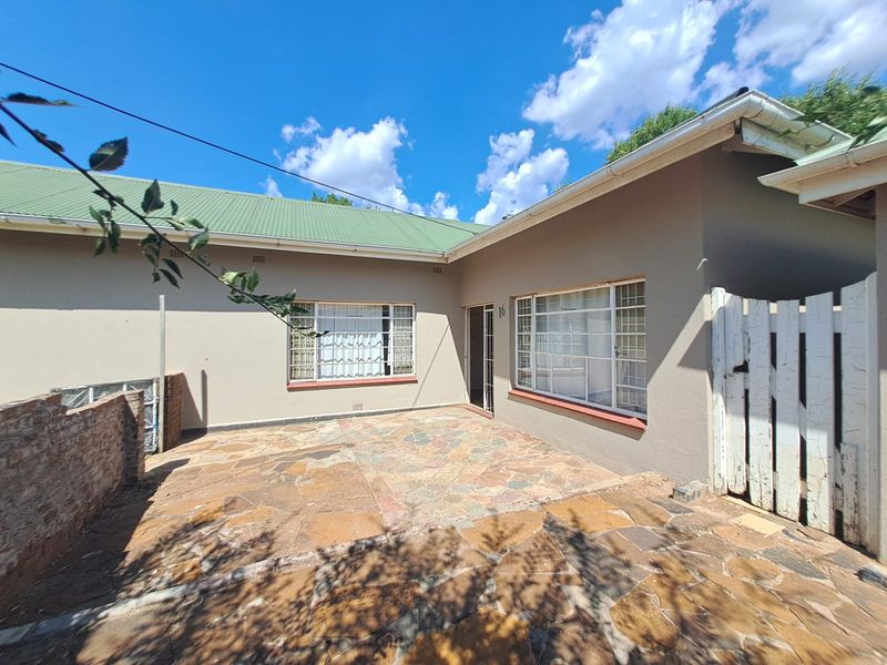 Rear exterior view of the property featuring a paved patio area, corrugated metal roofing, and secure window bars.