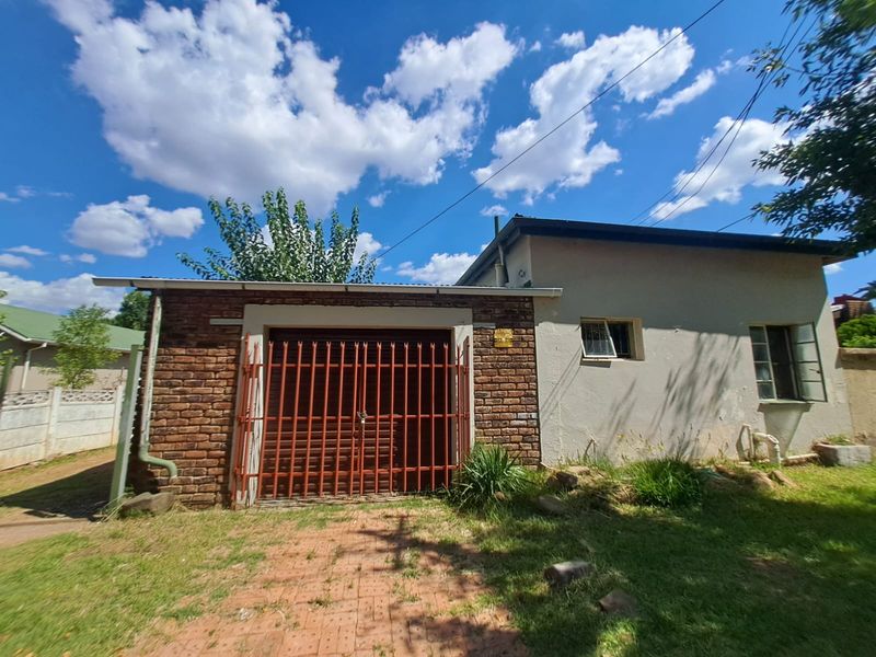 Front exterior view of a residential property featuring a brick garage section, metal security gate, and paved driveway area.
