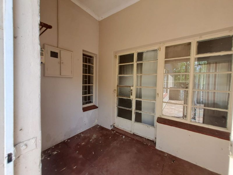 A covered patio area featuring steel-framed windows, a security gate, and an electrical distribution board, requiring minor cosmetic maintenance.
