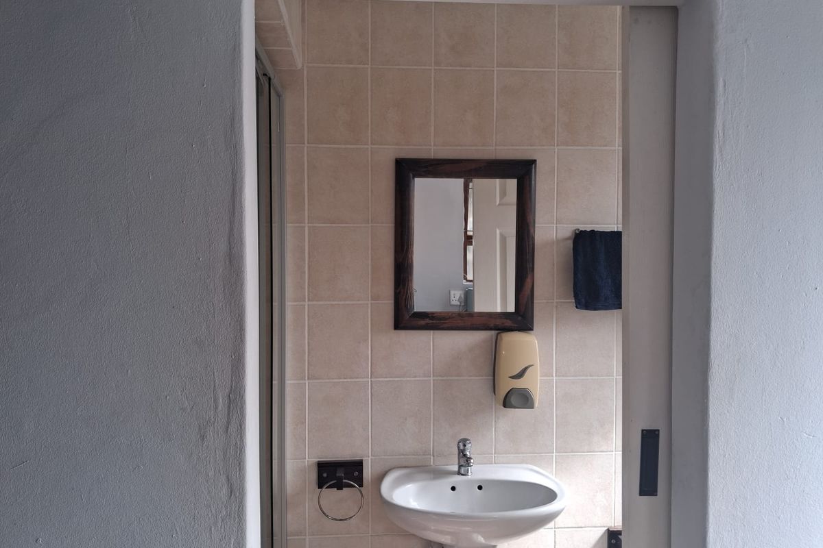 A functional bathroom featuring a pedestal basin, wall-mounted mirror, and neutral ceramic wall tiling.