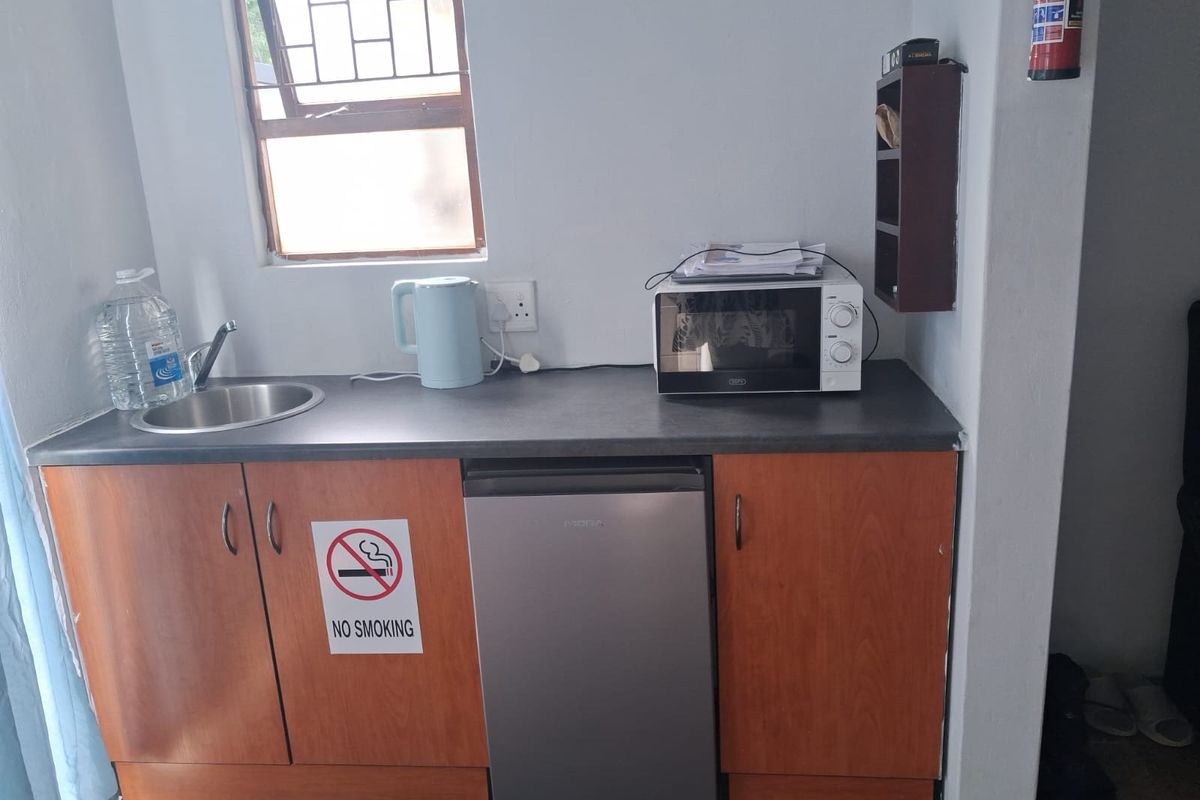 A compact kitchenette area featuring wooden cabinetry, a stainless steel sink, and a dark countertop, suitable for basic food preparation.