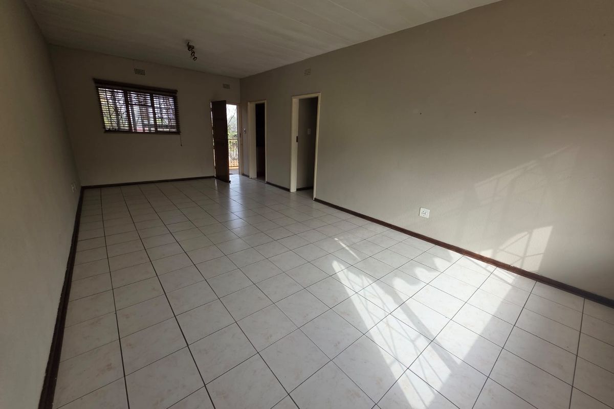 A spacious, empty living area featuring neutral tiled flooring, natural light, and direct access to adjacent rooms and an exterior balcony.