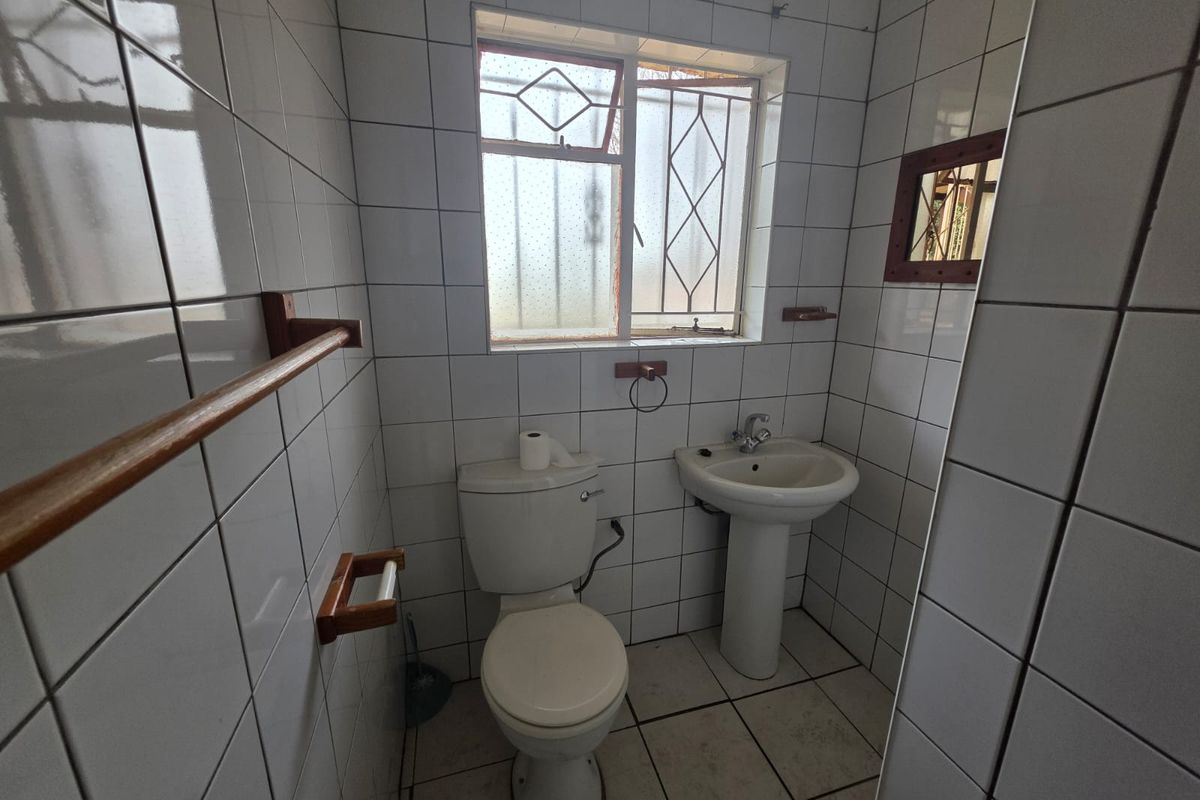 A compact bathroom featuring a pedestal basin, standard toilet, and floor-to-ceiling white wall tiling with a window for natural light.