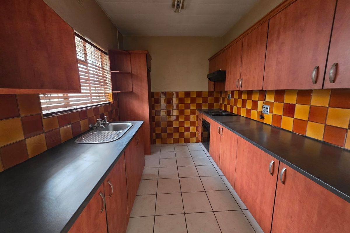 A galley-style kitchen featuring wooden cabinetry, dark countertops, and a distinctive checkered tile backsplash, offering a functional layout ready for modernization.