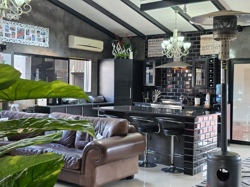 Spacious open-plan living and kitchen area featuring a modern kitchen island, dark subway tile backsplash, exposed ceiling beams, and polished tiled flooring.