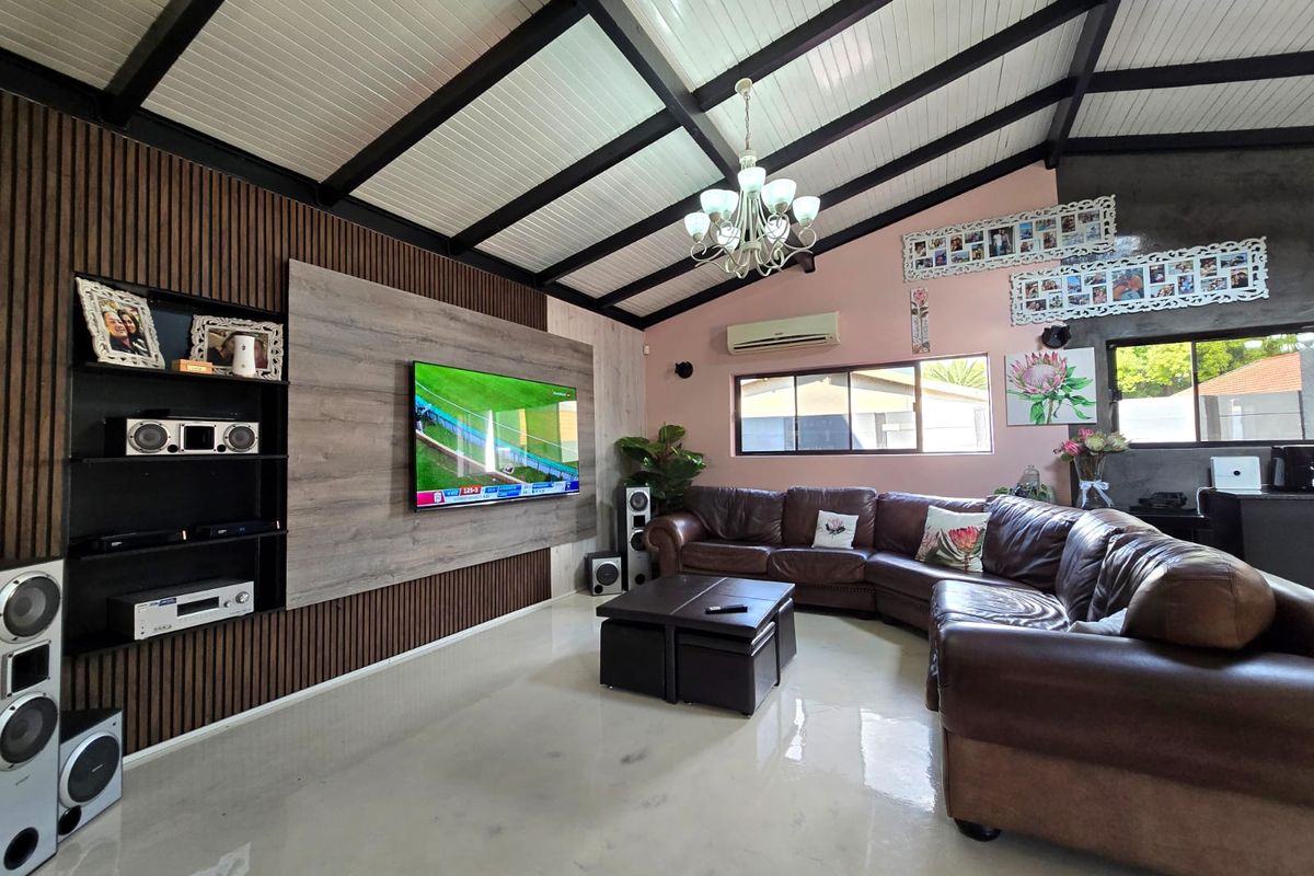 Spacious living room featuring a vaulted ceiling with exposed beams, polished concrete floors, and a modern slatted wood feature wall with integrated media space.