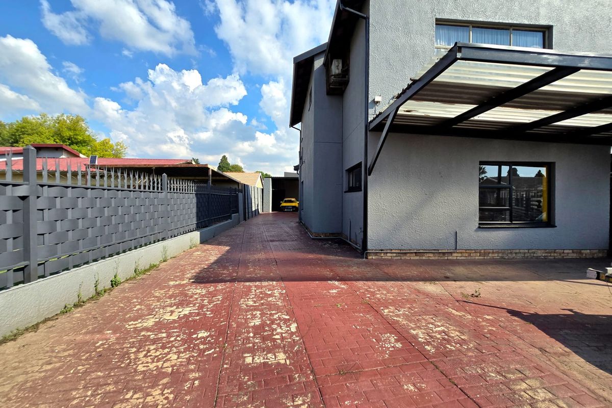 A side view of the property featuring a paved driveway with visible wear, metal perimeter fencing, and a covered patio area attached to the main structure.