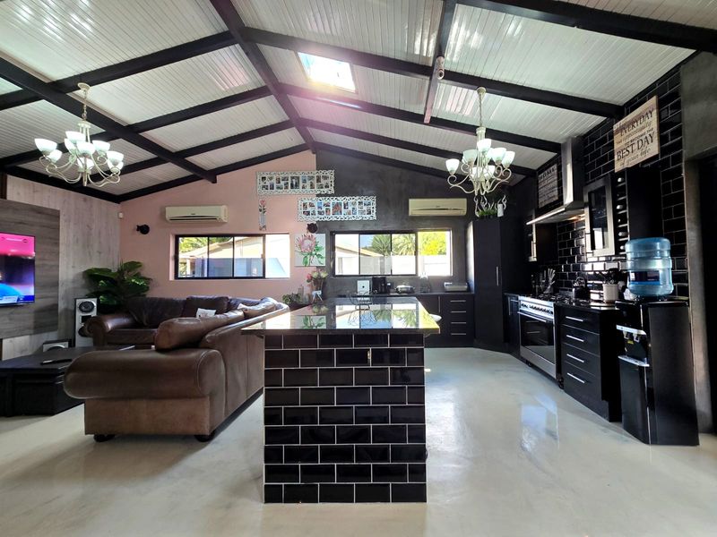 Spacious open-plan living and kitchen area featuring a vaulted ceiling with exposed beams, a central kitchen island, and modern black subway tile finishes.