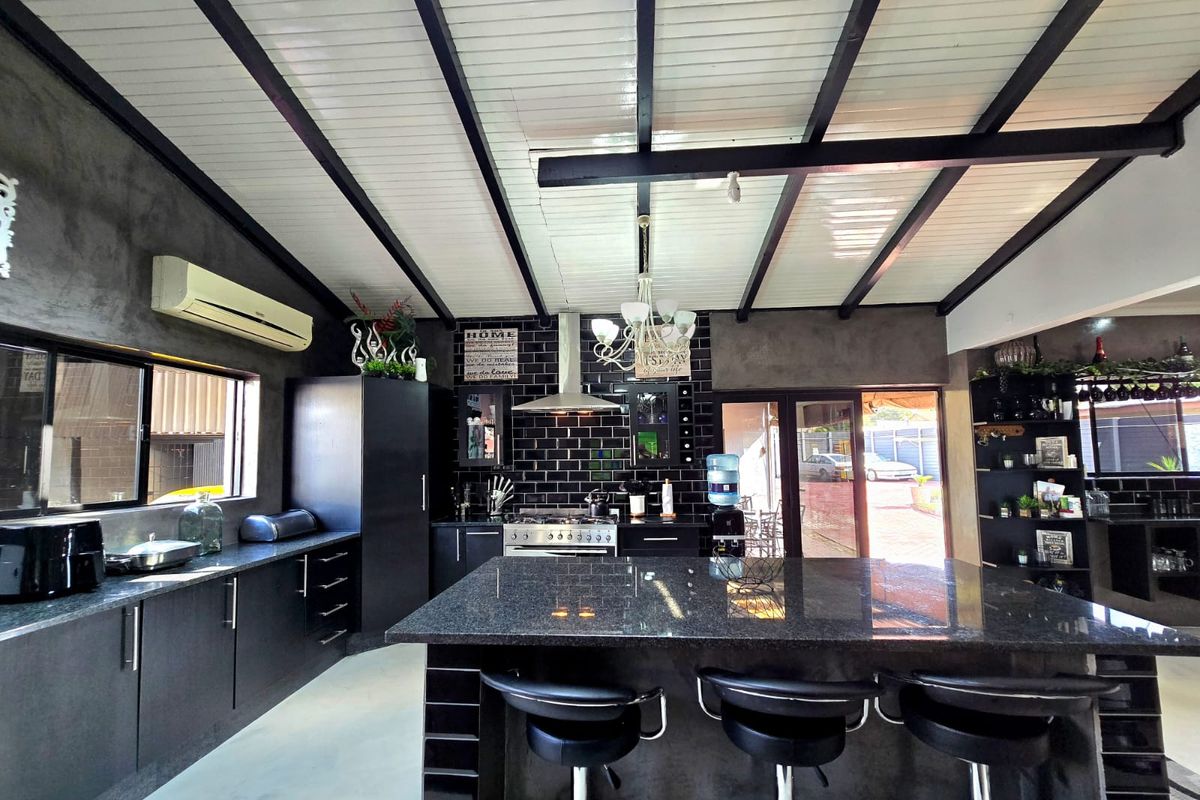 Modern kitchen featuring a large granite island, subway tile backsplash, stainless steel gas stove, and exposed ceiling beams with ample built-in cabinetry.
