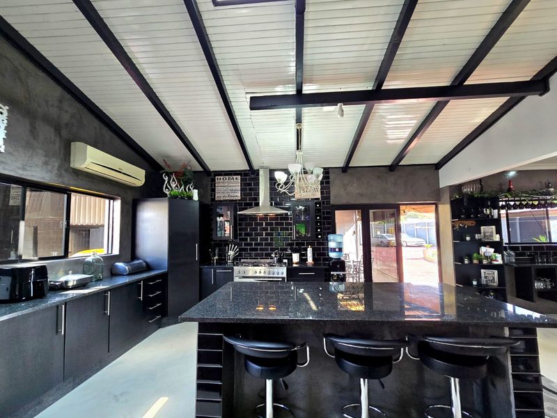 Modern kitchen featuring a large granite island, subway tile backsplash, stainless steel gas stove, and exposed ceiling beams with ample built-in cabinetry.