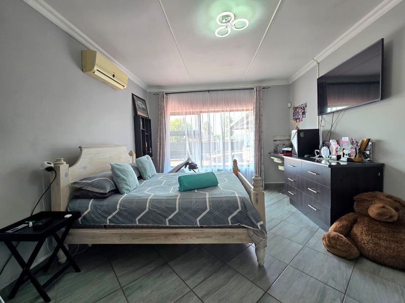 A bedroom featuring tiled flooring, crown molding, and a sliding glass door providing natural light, equipped with a wall-mounted air conditioning unit.