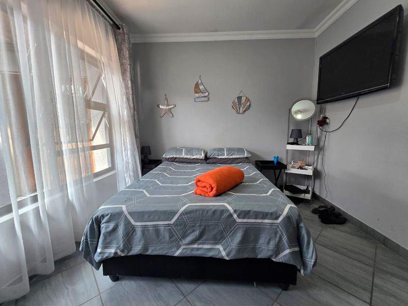 A functional bedroom featuring tiled flooring, neutral wall finishes, and a large window allowing for natural light.