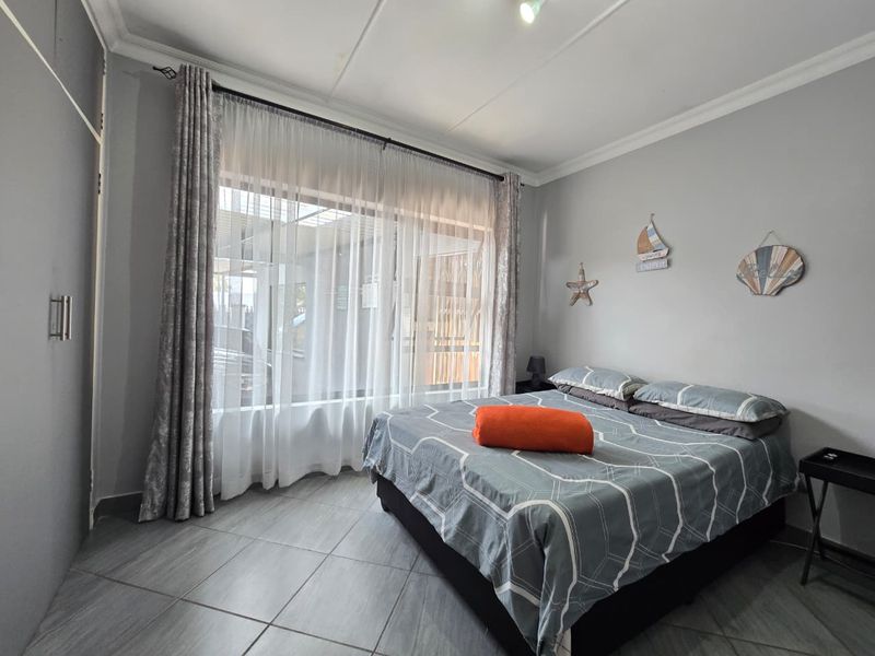 A well-maintained bedroom featuring tiled flooring, a built-in cupboard, and a large window that allows for ample natural light.