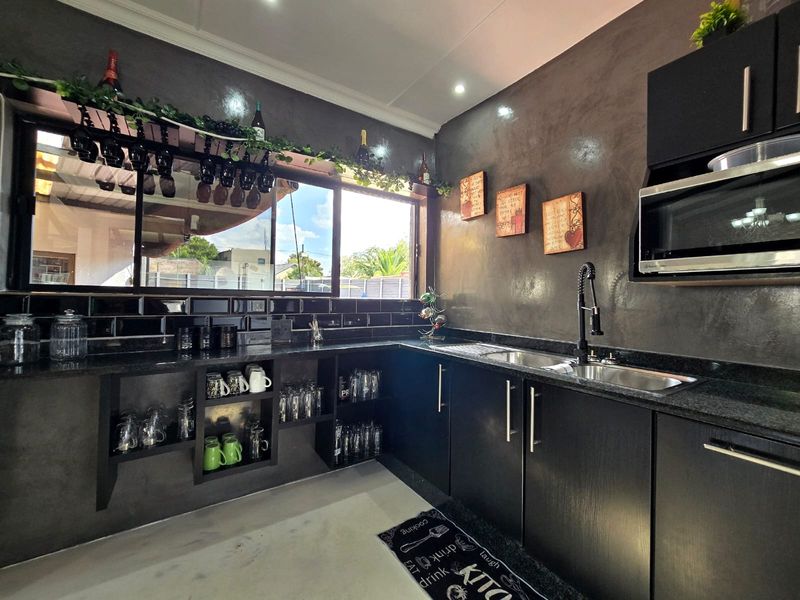 Modern kitchen featuring sleek black cabinetry, granite countertops, a stainless steel sink with a gooseneck faucet, and stylish black subway tile backsplash.