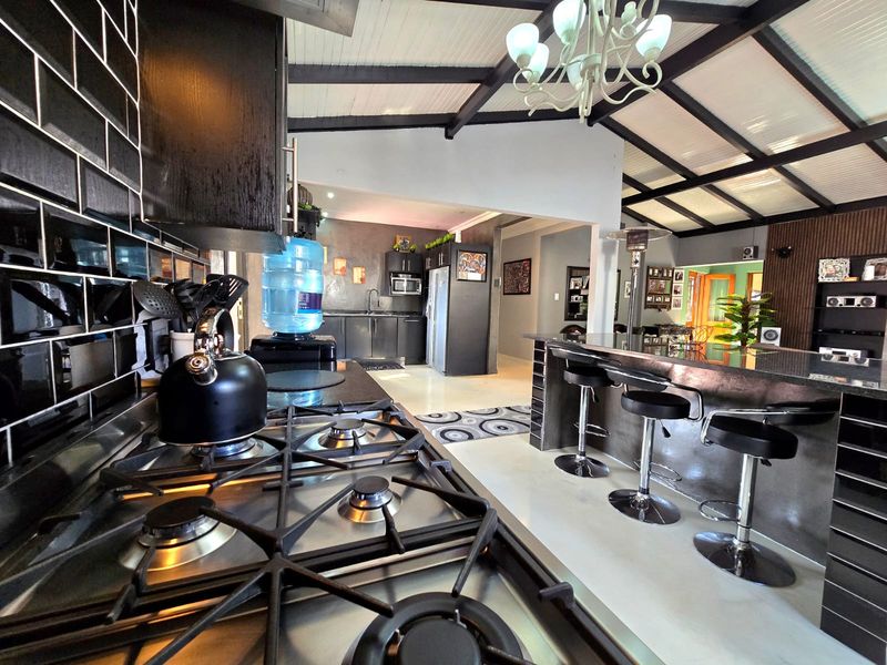 Spacious open-plan kitchen featuring a gas hob, subway tile backsplash, and a large central island with breakfast bar seating under an exposed beam ceiling.