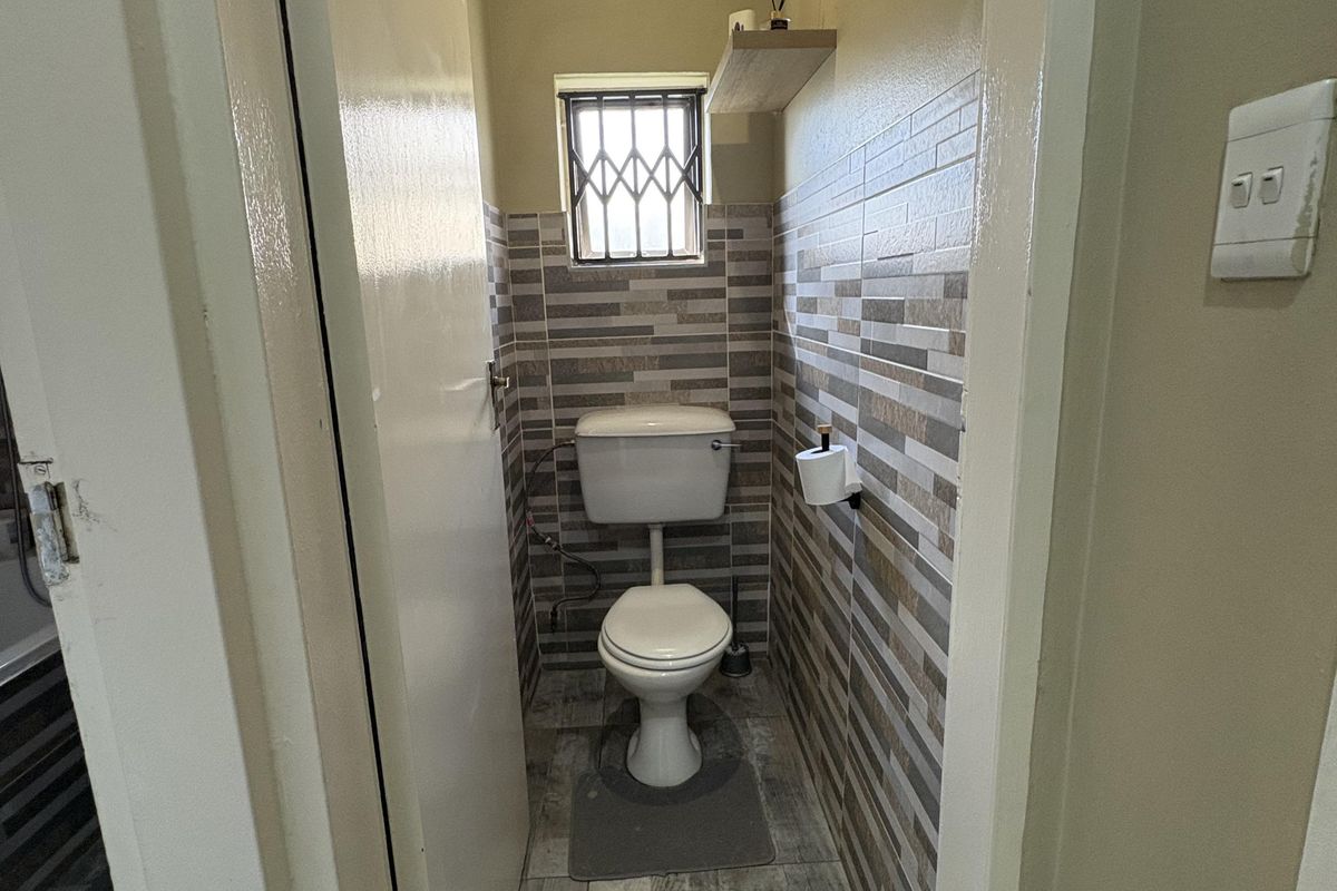 A compact guest toilet featuring tiled walls, wood-look floor tiles, and a security gate on the window.
