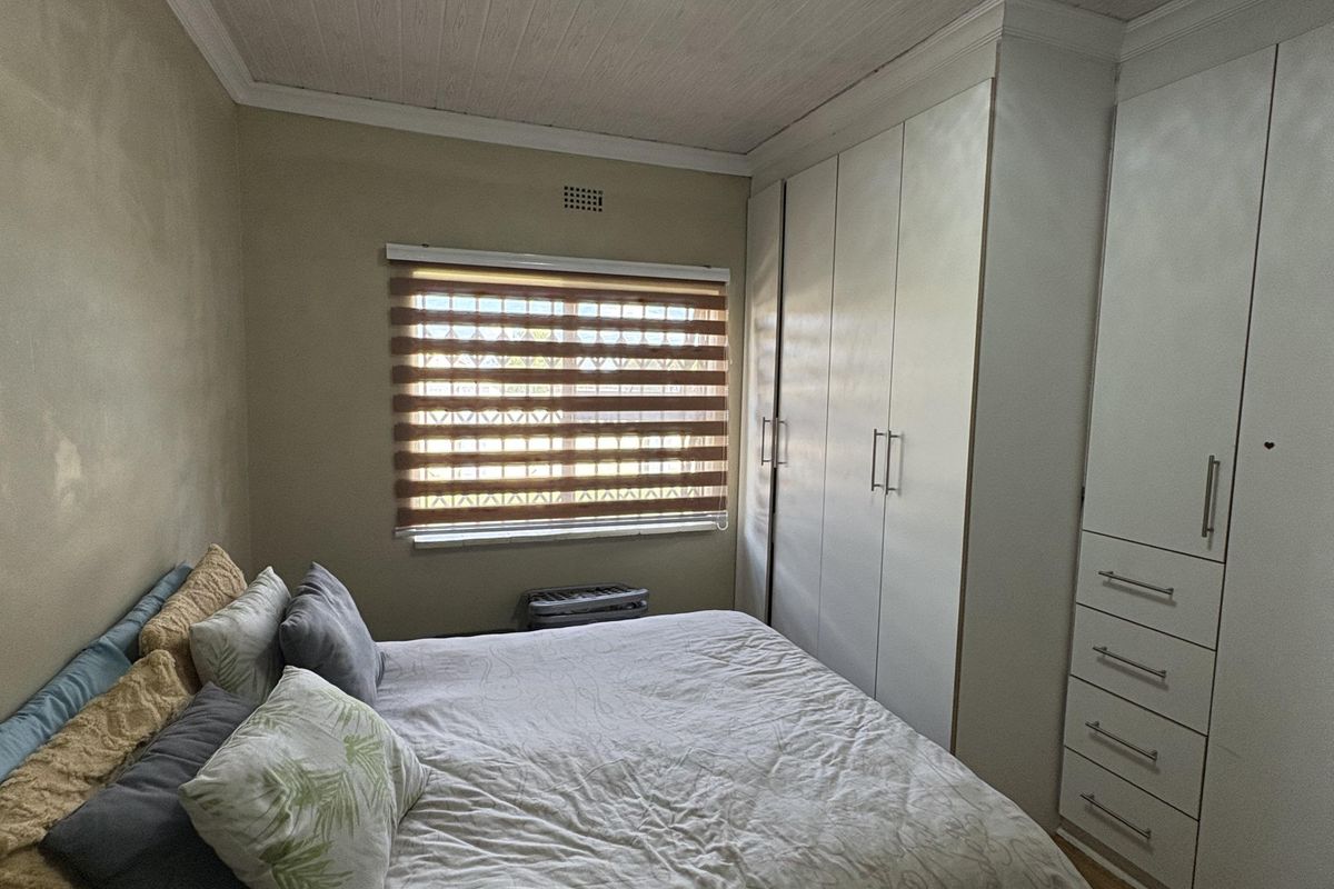 A well-maintained bedroom featuring built-in floor-to-ceiling wardrobes, wood-look flooring, and a timber-paneled ceiling with a modern flush-mount light fixture.
