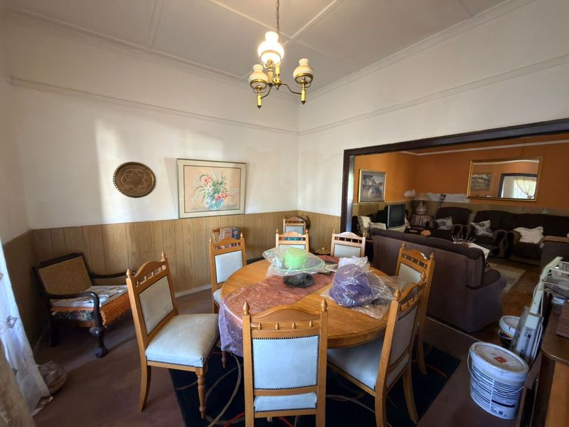 Dining room featuring timber wall paneling and a coved ceiling, opening into an adjacent living area.