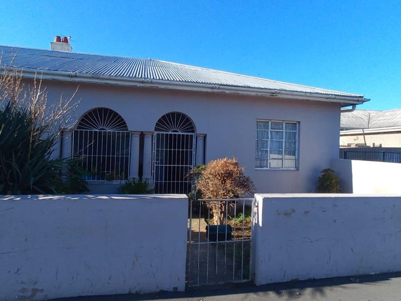 Front elevation of a single-story house featuring a corrugated metal roof, security gates, and a perimeter boundary wall.