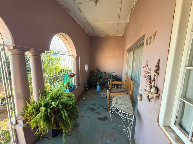 Covered patio area featuring arched columns, tiled flooring, and a sliding glass door entrance, showing signs of wear on the ceiling and walls.