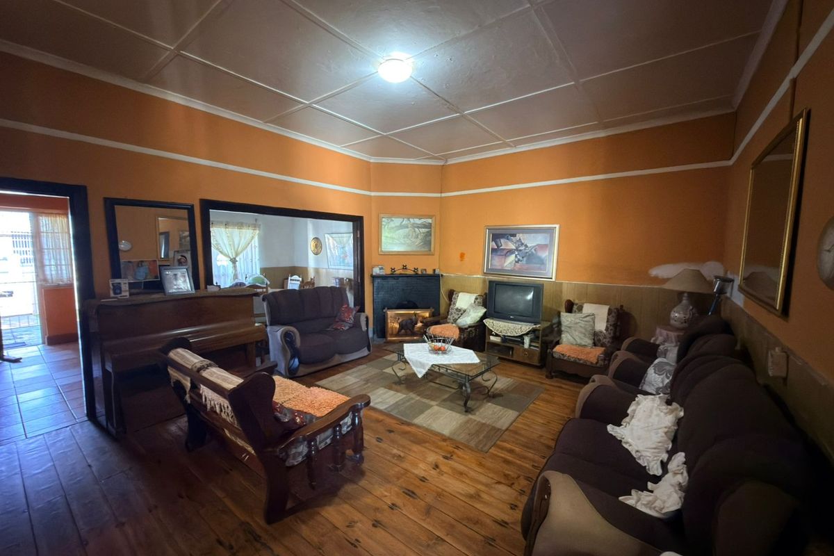 Spacious living room featuring original hardwood flooring, a fireplace, and a traditional tiled ceiling, offering a classic layout with potential for modernization.