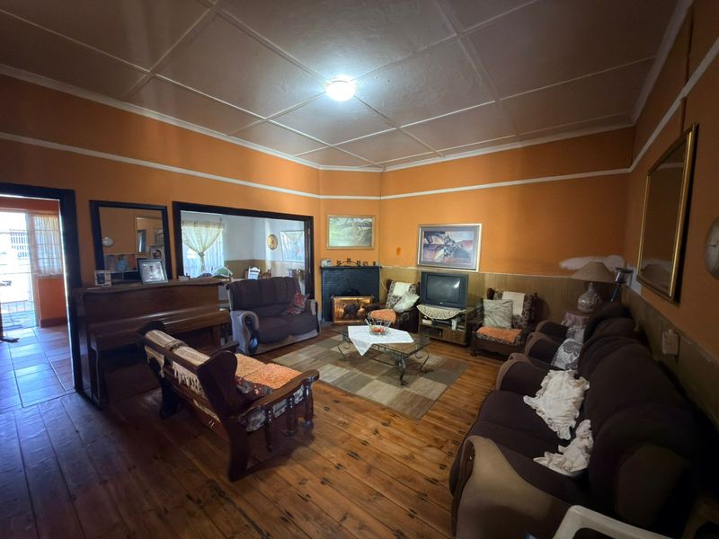 Spacious living room featuring original hardwood flooring, a fireplace, and a traditional tiled ceiling, offering a classic layout with potential for modernization.
