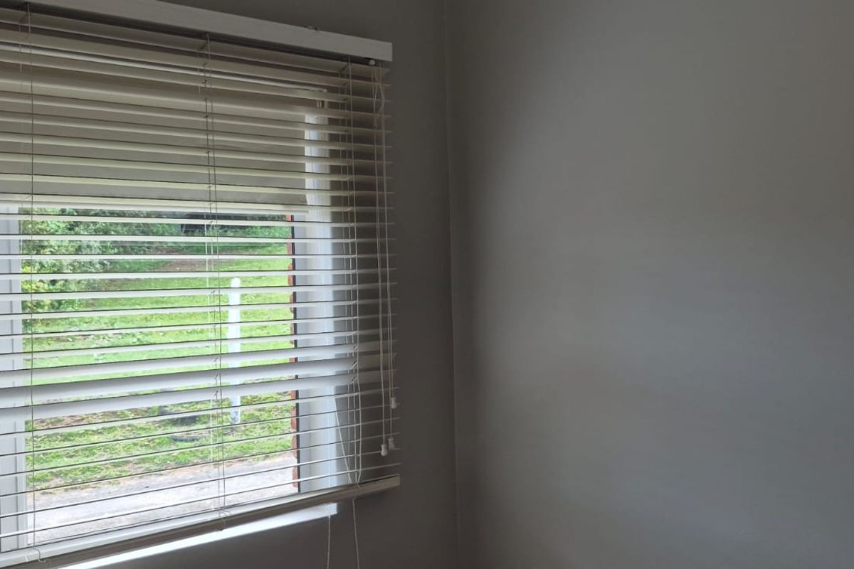 A simple bedroom corner featuring a window with fitted venetian blinds and neutral wall finishes.