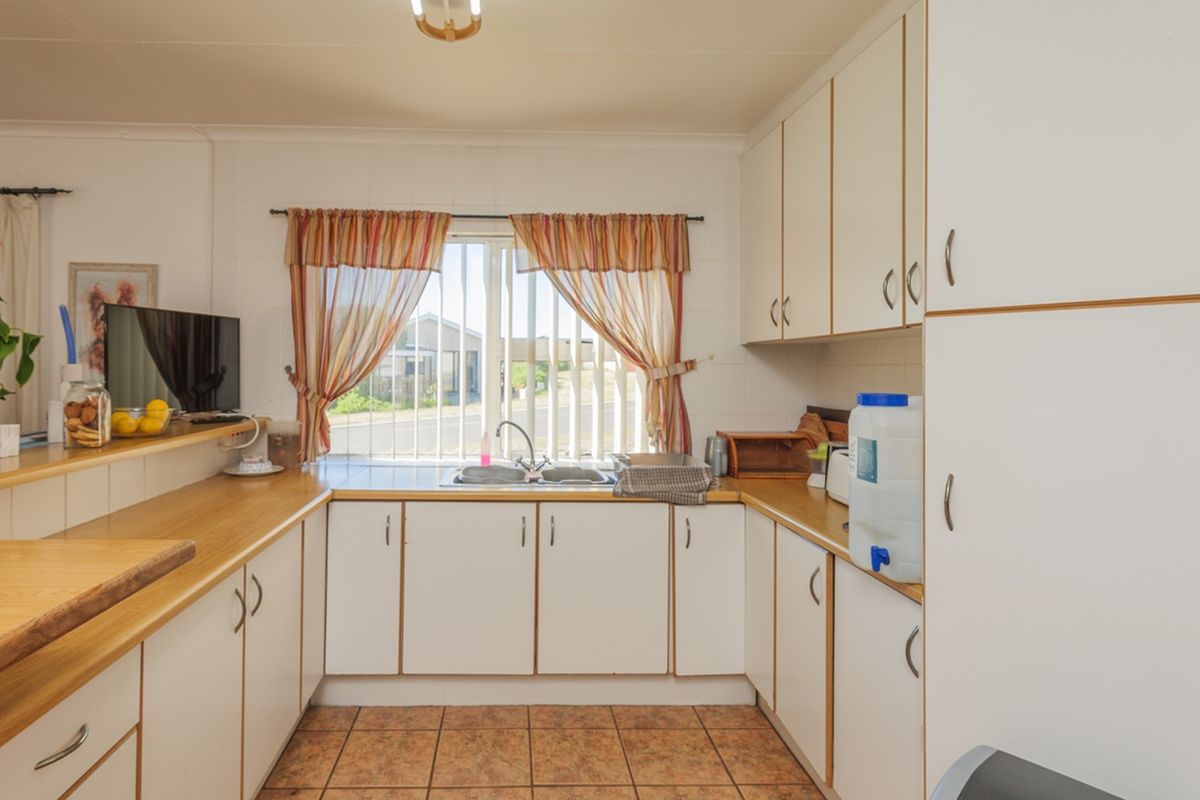A functional U-shaped kitchen featuring white cabinetry, laminate countertops, a double bowl sink, and tiled flooring with natural light from a window.